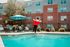 Inviting apartment complex pool area with cozy loungers and a vibrant mascot in front of modern brick buildings.
