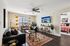 Bright living room with contemporary decor, featuring a cozy seating area, vibrant rug, and a wall-mounted TV. Dining table by a large window with stylish curtains, and a glimpse into a tastefully decorated bedroom.
