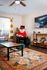Charming living room featuring a stylish rug, cozy seating area, and modern wall art, bathed in natural light from large windows with vibrant curtains.