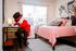 Inviting bedroom with a cozy workspace, featuring plush pink bedding, modern decor, and abundant natural light through large windows.