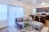 Modern open-concept living space featuring a cozy gray sofa, elegant glass coffee table, and stylish kitchen with dark wood cabinetry and bar seating.