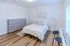 Bright and modern bedroom with sleek wood flooring, stylish grey dresser, and cozy double bed with crisp white linens, offering a serene and inviting atmosphere.