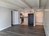 Modern apartment interior with sleek gray wood flooring, open doorway leading to a cozy kitchen featuring granite countertops and elegant white cabinetry.