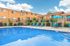 Inviting apartment complex with a refreshing swimming pool, vibrant blue lounge chairs, and umbrellas under a bright, clear sky.