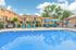 Inviting outdoor pool area with modern lounge chairs, vibrant umbrellas, and charming apartment complex backdrop under a clear blue sky.