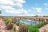 Charming apartment complex with a sparkling pool, surrounded by lush landscaping and scenic views under a bright blue sky.