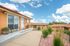 Charming brick apartment entrance with a cozy bench, vibrant potted flowers, and a welcoming pathway under a bright blue sky.
