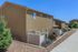 Modern townhouse with beige exterior, white fencing, and landscaped walkway on a sunny day.