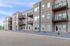 Modern three-story apartment building with stylish balconies and neatly landscaped surroundings under a clear blue sky.