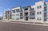 Contemporary apartment building with modern balconies, large windows, and ample parking, set against a clear blue sky.