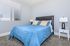 Inviting bedroom with plush carpeting, featuring a comfortable bed adorned with a vibrant blue quilt and decorative pillows, complemented by modern side tables and sleek lamps.