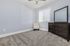 Bright and modern bedroom featuring plush carpet, an elegant armchair, large dresser, and abundant natural light from a sizable window with blinds.