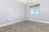 Bright and inviting empty room with soft carpeting, large window for natural light, and a neutral color palette.