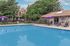 Inviting outdoor pool area with relaxing lounge chairs and vibrant purple umbrellas, surrounded by lush greenery and quaint residences.