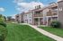 Charming apartment complex with wooden balconies, lush green lawns, and a clear blue sky backdrop.
