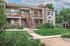 Charming apartment complex with spacious balconies, lush green landscaping, and a welcoming exterior staircase, perfect for comfortable living.