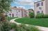 Charming apartment complex with beautifully manicured lawns, elegant beige siding, and a peaceful walkway under a bright blue sky.