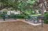 Charming outdoor picnic area with green benches and a grill, surrounded by lush greenery and residential buildings.