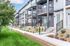 Modern townhomes with sleek balconies, surrounded by lush green lawns and landscaped gardens, under a clear blue sky.
