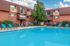 Inviting apartment complex featuring a sparkling swimming pool with vibrant blue lounge chairs and a charming brick facade under a sunny sky.