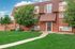 Charming brick apartment building with tidy landscaping and lush green lawn, offering a welcoming entrance under a clear blue sky.