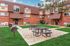 Charming apartment building with a welcoming brick exterior, surrounded by lush green grass, featuring picnic tables and outdoor grills for entertaining.