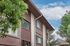 Charming apartment building with stylish wooden accents, nestled among lush greenery and under a clear blue sky.