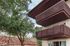 Charming apartment with modern wooden balconies, surrounded by lush greenery and red stone landscaping for an inviting natural ambiance.