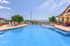 Inviting outdoor pool area with sun loungers and lush greenery, perfect for relaxation and leisure under a clear blue sky.