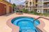 Inviting outdoor hot tub area with safety railing, surrounded by modern apartment architecture and green landscaping, perfect for relaxation.
