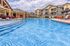 Inviting outdoor pool area with crystal clear water, surrounded by elegant apartment buildings and relaxing lounge chairs under a sunny sky.