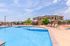 Luxurious apartment complex featuring a pristine outdoor pool, ample lounge chairs, and vibrant landscaping under a clear blue sky.