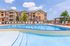 Luxurious apartment complex with a sparkling pool, stylish lounge chairs, and vibrant landscaping under a sunny sky.
