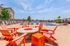 Inviting outdoor lounge area with vibrant orange chairs and a modern fire pit, overlooking a sparkling blue pool under sunny skies.