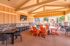 Inviting outdoor community lounge with vibrant orange seating, wall-mounted TV, and modern grilling stations under an elegant wooden ceiling.