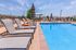 Luxurious apartment complex with a sparkling outdoor pool and stylish sun loungers under a clear blue sky.