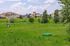Charming suburban landscape with vibrant green lawns, scenic trees, and contemporary apartment buildings in the background under a bright blue sky.