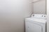 Modern laundry room with a sleek white washing machine and overhead shelving, enhancing convenience and efficiency.