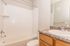 Bright and pristine bathroom featuring a modern vanity with granite countertop, polished chrome faucet, and a sleek tiled bathtub.