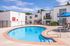 Inviting apartment complex with a sparkling blue pool, spacious patio, and modern architecture under a bright sky.