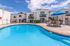 Inviting apartment complex showcasing a pristine swimming pool, sun loungers, and charming balconies under a bright blue sky.