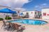 Inviting apartment complex pool area with blue umbrellas, sun loungers, and modern architecture under a bright sky.