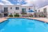 Inviting residential pool area with lounge chairs and umbrella, surrounded by modern white buildings under a stunning blue sky.