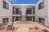 Charming apartment complex featuring a sunlit courtyard with modern patio seating and decorative plants, framed by elegant white exteriors and large windows.