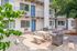 Charming apartment courtyard with modern outdoor seating and BBQ area, surrounded by lush greenery and vibrant blue doors.