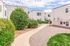 Charming apartment exterior with white stucco walls, lush greenery, and a bright, inviting walkway under a clear blue sky.