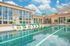 Luxurious apartment community featuring a sparkling pool with modern lounge chairs, vibrant seating, and expansive glass windows under a clear blue sky.