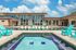 Luxurious apartment complex with modern architecture, featuring a sparkling swimming pool, jacuzzi, and vibrant turquoise lounge chairs under a bright blue sky.