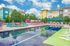 Vibrant apartment complex with a colorful poolside featuring modern lounge chairs, surrounded by lush greenery and contemporary buildings under a bright blue sky.