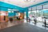 Modern fitness studio with vibrant teal walls, sleek wood flooring, exercise bikes, and large windows overlooking a sunlit patio.